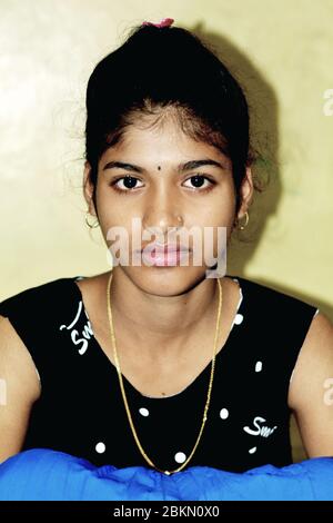 Close up of an Indian teenage girl sitting in solidarity posing for the camera wearing a black dress, selective focusing Stock Photo