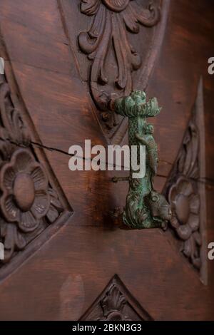 A metal door knob with a green patina and the head of a lion. A dark wooden carved  textured background in the old town of Dubrovnik, Dalmatia, Croati Stock Photo