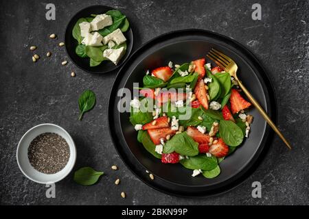 Top view of a black plate with strawberry spinach salad and its ingredients Stock Photo