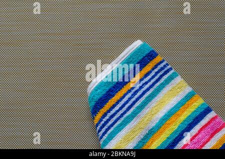 Multi-colored striped beach towel close-up. Colorful rainbow colored towel on a light brown textured background. Positive colors. Abstract background. Stock Photo