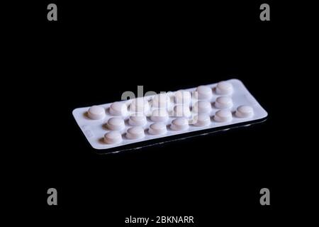 A white foil strip with medicine tablets, displayed on a black table Stock Photo