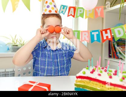The boy put the balloons to his eyes. Birthday party and cake at home Stock Photo