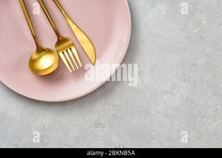 Flat lay of pink plate and gold cutlery on grey background Stock Photo