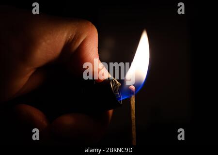 Lighting a match stick with a lighter isolated on a black background Stock Photo