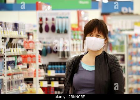 Woman in medical mask in a mall on background of shelves with goods. Concept of shopping during quarantine at covid-19 pandemic Stock Photo