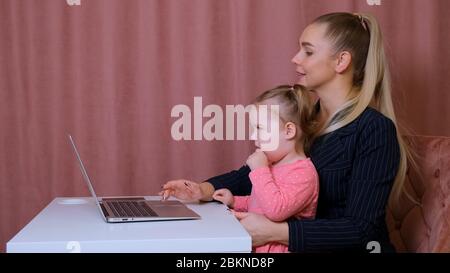 Working mom works from home office. Happy mother and daughter smiling. Successful woman and cute child using laptop. Freelancer workplace. Female Stock Photo