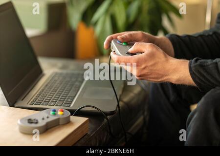 A man playing on his laptop computer with a old school classic gaming console feeling nostalgic at home during lockdown time in 2020 Stock Photo