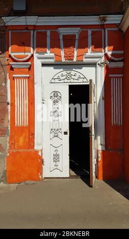 White door decorated by curly pattern gratings and lattice. Opened door of orange painted building with fake column. Classic architecture of European Stock Photo