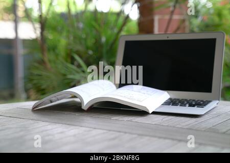 Open book on top of computer laptop. Garden view. Home setting. Onlien education concept. Stock Photo