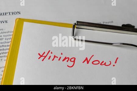 Hiring Now, words in red on white paper on a file clipboard. Employment concept. Stock Photo