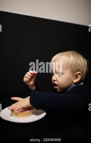A little blond boy eats sweets. Delicious tartlet. Stock Photo