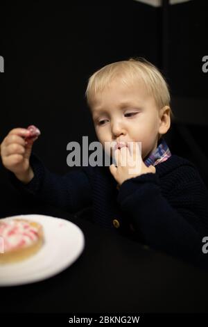 A little blond boy eats sweets. Delicious tartlet. Stock Photo