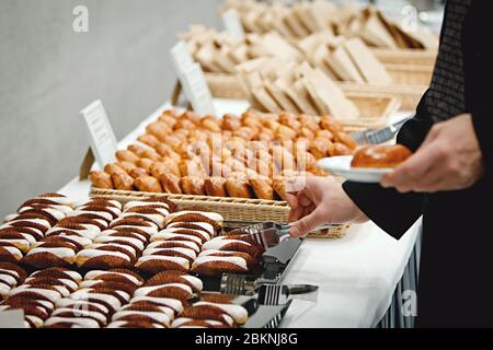 A man in black suit whose face can not be seen takes a custard cake from a banquet table with metal tongs Stock Photo