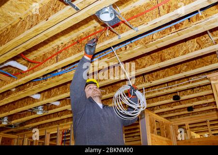 Construction worker electrician wiring lights on ladder inside