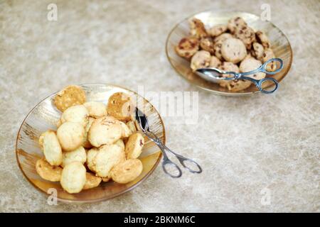 Cookies lying in two plates with food tongs on a marble table Stock Photo