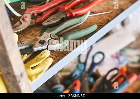 Old instruments such as wire cutters, diagonal pliers, garden scissorson and working gloves on a shelf in garage Stock Photo