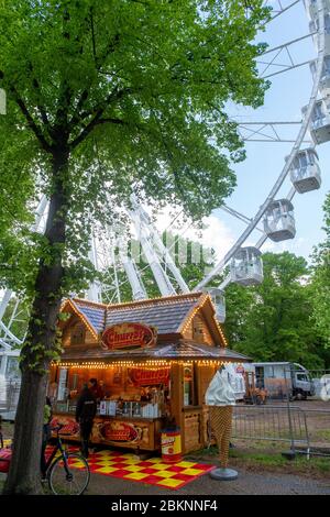 05 May 2020, Saxony-Anhalt, Magdeburg: A Ferris wheel stands between the trees of Rotehorn Park. Currently, the operators are working out a concept to comply with the distance rules. At the base a snack bar has already opened and sold diner. However, eating is not allowed within a radius of 50 meters. The Ferris wheel had been set up in the past weeks and is operated by the Boos brothers from Magdeburg. Actually the ride should have been operated at other fairs at the moment. But they had been cancelled due to the spread of the corona virus. Now the Ferris wheel is in the state capital and is Stock Photo