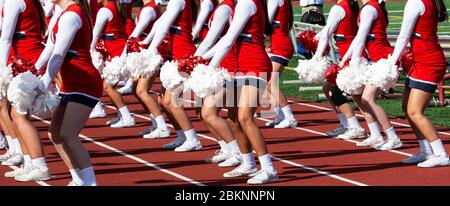 High school cheerleaders in red and white uniforms performing for the crowd during homecoming football game. Stock Photo