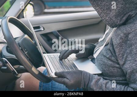 Hooded thief tries to break the car's security systems with laptop. Hacking modern car concept Stock Photo