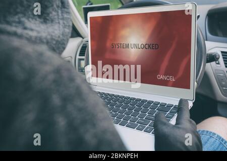 Hooded thief tries to break the car's security systems with laptop. Hacking modern car concept Stock Photo