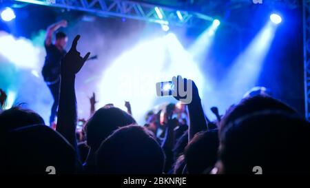 Unrecognizable hands silhouette taking photo or recording video of live music concert with smartphone. People partying in front of the stage Stock Photo