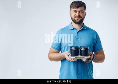 Man coffee shop worker giving takeaway cups of coffee on grey background Stock Photo