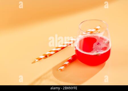 Pink alcoholic cocktail with lemonade, champagne or Martini decorated with dry rosebuds on colored background with glare in the background Stock Photo
