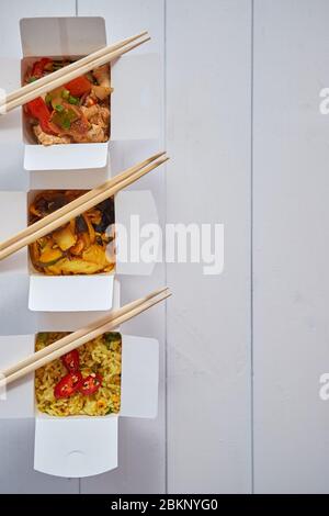 Three take away paper boxes filled with asian food placed in row on white Stock Photo