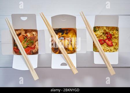 Three take away paper boxes filled with asian food placed in row on white Stock Photo