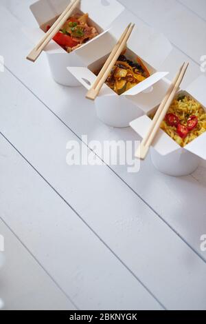 Three take away paper boxes filled with asian food placed in row on white Stock Photo