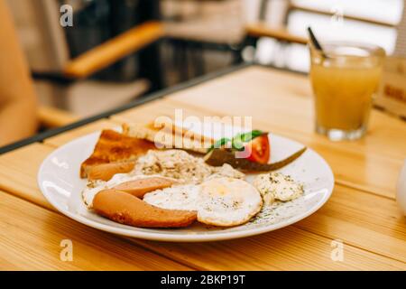 Delicious breakfast in the cafe: scrambled eggs and a glass of juice. Scrambled eggs with sausages, tomatoes and cheese. Scrambled eggs with ham and t Stock Photo