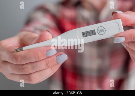 Woman hands showing digital medical thermometer with high temperature - close up, selective focus. Healthcare, measurement, disease, covid 19 Stock Photo