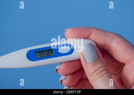 Woman hands holding white digital medical thermometer with high temperature - close up view, selective focus. Healthcare, measurement, disease Stock Photo