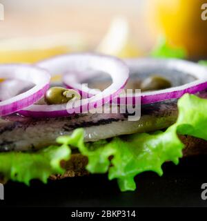 Appetizing smorrebrod with Norwegian herring, lettuce, blue onion, lemon and tomato lies on a wooden board Stock Photo