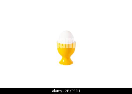 White egg standing on yellow egg cup, isolated on white background. Copy space. Stock Photo