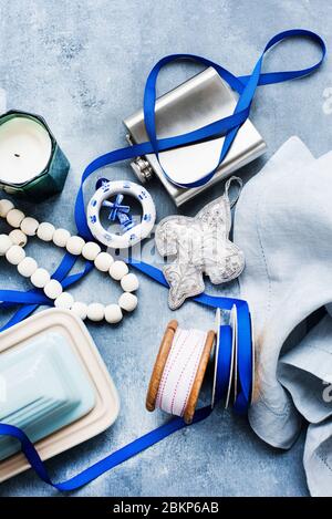 Overhead view of blue and white ribbons, silver hip flask, butter dish, white beads and a grey linen napkin. Stock Photo