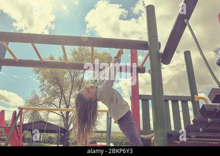 Little girl playing on playground, hanging walk along the monkey bars. Stock Photo