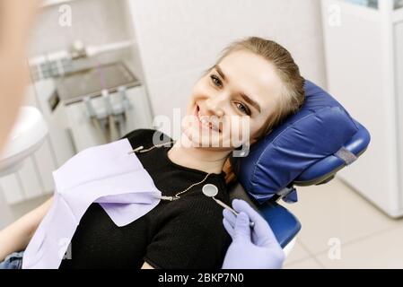 Smiling and satisfied patient in a dental office after treatment. Young female sitting in dentist office and looking at her doctor with smile. Stock Photo