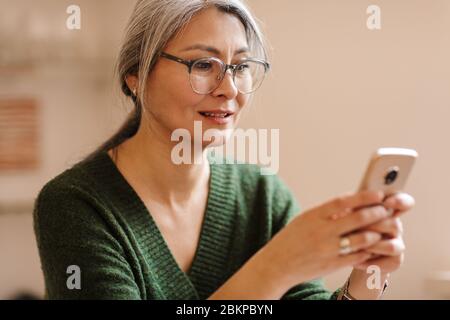 Image of amazing pleased mature beautiful grey-haired woman indoors using mobile phone. Stock Photo