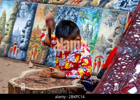 A Local Child Artist Working With Leather At The Banteay Kdei Temple, Angkor Wat Temple Complex, Siem Reap, Cambodia. Stock Photo