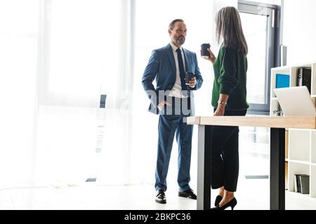 Photo of adult serious colleagues discussing project and drinking coffee while working in office Stock Photo