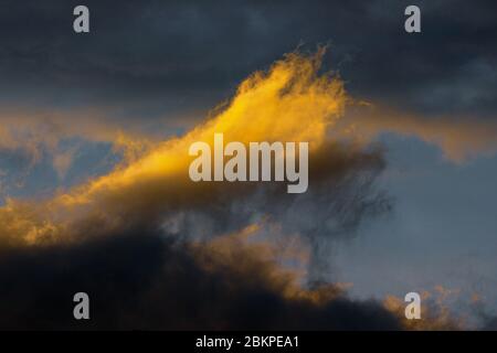 Stunning fluffy thunderstorm clouds illuminated by disappearing rays at sunset and dark thunderclouds floating across sunny blue sky to change season Stock Photo