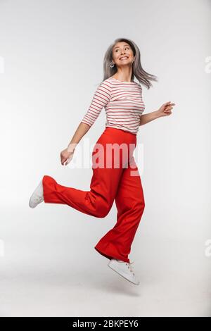 Portrait of an elegant smiling beautiful mature lady with long gray hair wearing casual clothes jumping isolated over background Stock Photo