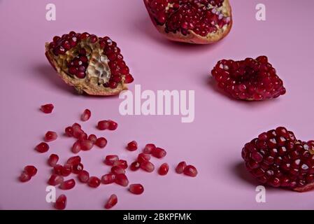 Broken red ripe pomegranate fruit on the pastel pink background. Selective focus. Stock Photo