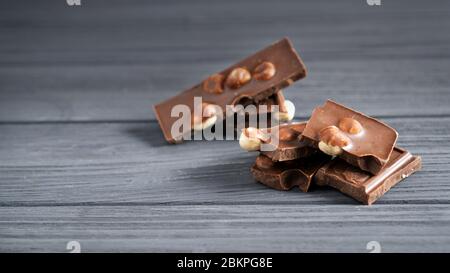 Pieces of milk chocolate with nuts on a gray wooden table. Chocolate bars with hazelnut. Sweet brown chocolate stack. Stock Photo