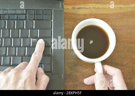 finger pushing enter button on computer notebook while holding coffee cup Stock Photo