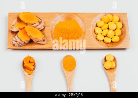 Turmeric in different conditions: dry root, tablets, powder and cut plant. It is on wooden tray with spoons. Flat lay style. Stock Photo