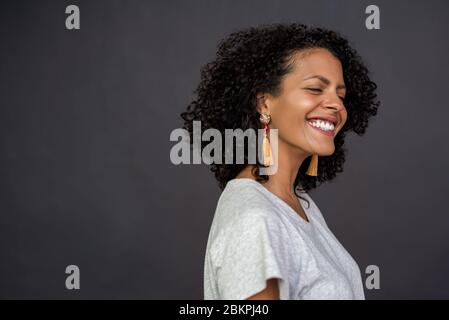 Laughing young woman standing with her eyes closed on gray Stock Photo