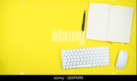 directly above shot of computer keyboard, mouse and note pad on yellow desk Stock Photo