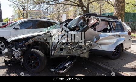 a totaled, abandoned car half on the sidewalk, half on the street. Silver color body with the exploded airbag visible through the smashed window Stock Photo